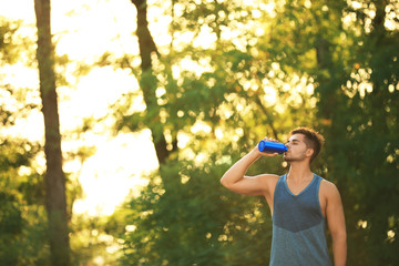 Young man drinking water from sport bottle after training in park