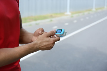Young man checking pulse with medical device after training, closeup