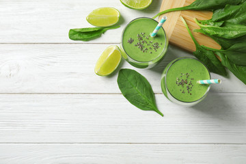 Glasses of healthy green smoothie with fresh spinach on white wooden table, flat lay. Space for text