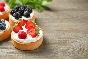 Different berry tarts on wooden table, space for text. Delicious pastries