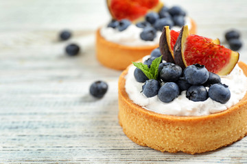Tarts with blueberries and figs on white wooden table, space for text. Delicious pastries