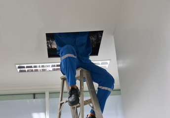 Technician sitting on ladder while working in the opening ceiling