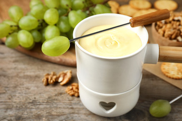 Fondue pot with white chocolate and grapes on wooden table, closeup
