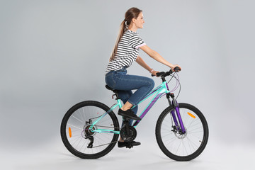 Happy young woman riding bicycle on grey background