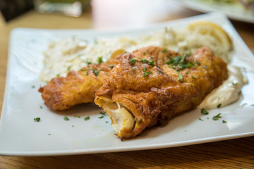 Seelachs Backfisch im Bierteig mit Remoulade, Kartoffelsalat und Krautsalat auf Holztisch 