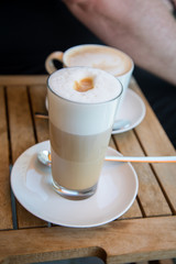 Glas Latte Macchiato und Tasse Cappuccino Kaffee mit Milchschaum auf Holztisch draußen im Straßencafé 