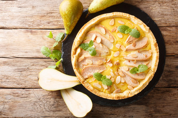 Homemade fresh pear tart with custard, almonds and mint closeup on a slate board. Horizontal top view