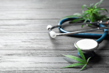 Hemp leaves and stethoscope on grey wooden table. Space for text