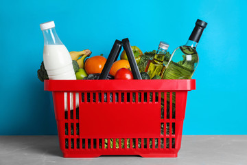 Shopping basket with grocery products on grey table against light blue background