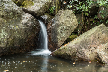 Fototapeta na wymiar beautiful waterfall run down the crack of big rocks at the end of the creek inside forest