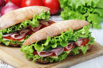 Two sandwiches with fresh vegetables, ham and cheese in ciabatta bread	