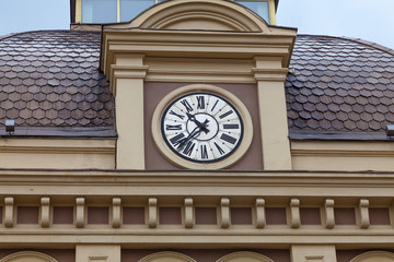 Clock above the entrance to the train station with a fragment of the roof, covered with brown metal tiles