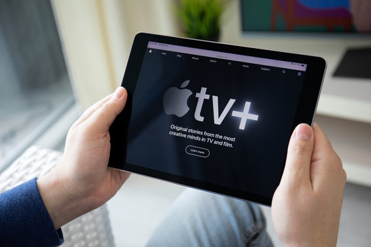 Man holding iPad with Apple TV app provides streaming movies.
