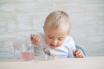 A little boy with a genetic disease Down Syndrome is sitting at the table and eating. The child...