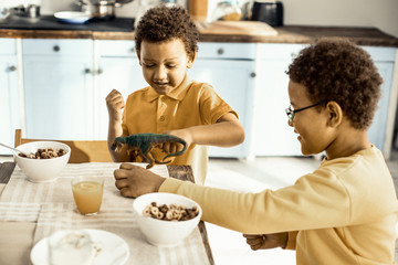 Twins are trying to feed the toy with flakes during morning get-together.