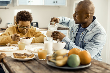 Kid choosing milk for breakfast, and dad pouring him a glass.