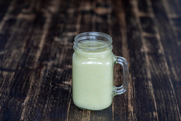 Fresh green smoothie from avocado, banana and honey in glass mug on wooden background, closeup. Concept of healthy eating