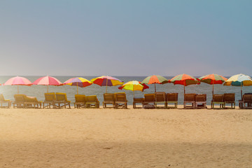 Row of covered wooden deck chairs with colorful umbrellas on the beach in GOA, India, toned. Sea summer template. Long shot.