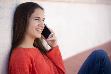 Chica adolescente feliz hablando por teléfono móvil sentada en