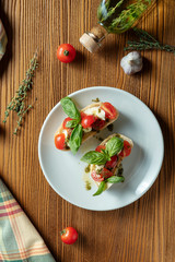 bruschetta with cherry tomatoes, basil, pesto sauce and mozzarella on a white plate on a wooden background. Italian restaurant. Top view food photo