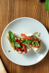 bruschetta with bell pepper, basil, pesto sauce and mozzarella on a white plate on a wooden background. Italian restaurant. Top view food photo
