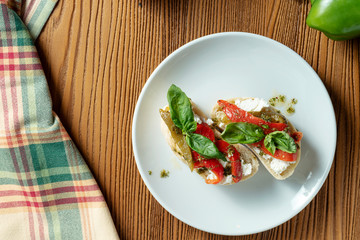 bruschetta with bell pepper, basil, pesto sauce and mozzarella on a white plate on a wooden background. Italian restaurant. Top view food photo