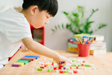 A little asian boy learning about numeracy, adding - subtracting and counting through colorful cuisenaire rods. Early math, Cognitive skills, Learning tools, Child development, Educational concept.