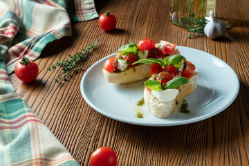 bruschetta with cherry tomatoes, basil, pesto sauce and mozzarella on a white plate on a wooden background. Italian restaurant. Top view food photo