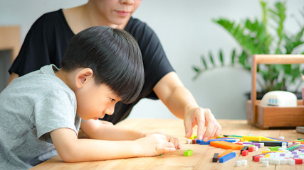Cute kindergarten Asian boy learning with mother about numeracy, adding - subtracting and counting through colorful cuisenaire rods. Early math, Cognitive skills, Problem solving, Child development.