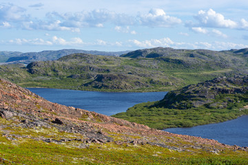 Beautiful hilly landscape. Fluffy clouds fly over the ancient hills, hills cut the azure water surface. Peaceful and tranquil mood reigns in these places. Murmansk region, Russia