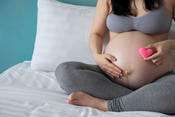 pregnancy, motherhood and expectation concept - smiling pregnant woman touching big belly on bed.