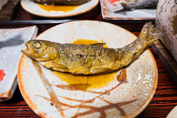 Iwana fish or Salvelinus grilled on a plate topped with Japanese sauce water on table and food set.