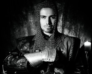 Portrait of handsome knight in suit of armour looking at camera with candles in background