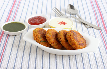 Kabuli chana tikkis, or chickpea patties, a healthy, vegetarian, delicious, and Indian food, with green chutney, ketchup, and curd with a topping of chili powder.