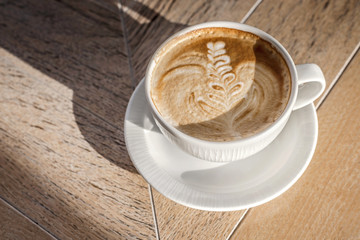 White big cup of cappuccino with art on wooden table with shadow and copy space.