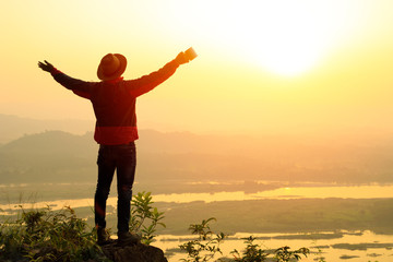 Male tourists standing arms spread, Man enjoying with the top of the mountain. Morning coffee, Thailand, Young man with hands up on sunrise background, concept of travel and freedom