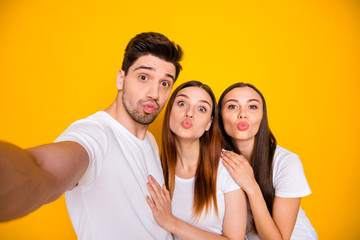 Self-portrait of three nice attractive lovely lovable charming cheerful cheery positive person sending you kiss having fun isolated over bright vivid shine yellow background