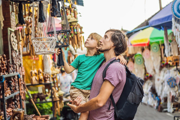 Dad and son at a market in Ubud, Bali. Typical souvenir shop selling souvenirs and handicrafts of Bali at the famous Ubud Market, Indonesia. Balinese market. Souvenirs of wood and crafts of local