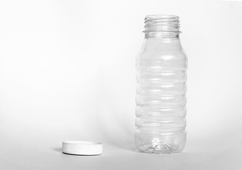 empty transparent open plastic bottle without cap, cap lies next to a white background, the concept of debris removal