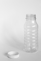 empty transparent open plastic bottle without cap, cap lies next to a white background, concept of debris removal