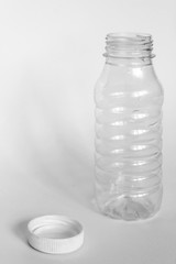 empty transparent open plastic bottle without cap, cap lies next to a white background, concept of debris removal