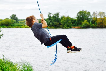 Cheerful boy swinging on a rope swing above the water.