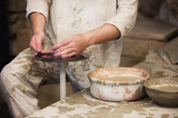 Man working with fresh wet clay on pottery wheel. Male hands make a ceramic plate the old way in the workshop