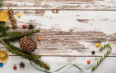 Christmas decor, top view with free space. On a light wooden table, a fir branch with a pine cone, multi-colored sweets, cinnamon sticks and anise.