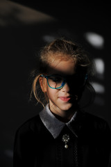 Fototapeta na wymiar unique young caucasian person wunderkind little girl in glasses and school black and white uniform smiling in darkness