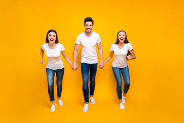 Fototapeta premium Full length photo of cheerful people holding hands enjoying screaming isolated over yellow background