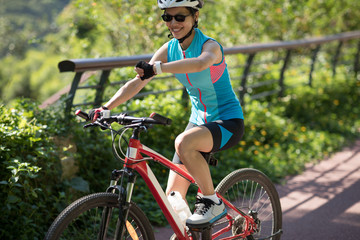 Fototapeta na wymiar Woman riding on park bike path, looking at her smartwatch while riding bike on sunny day