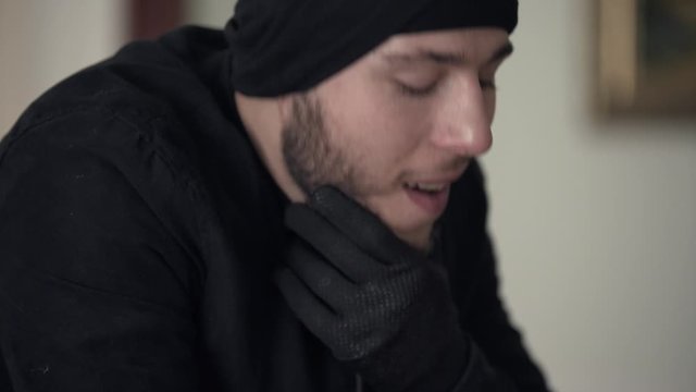 Close-up of young caucasian thief in black clothes thinking on the next crime. The guy stealing things in rich house. Concept of offense against the law