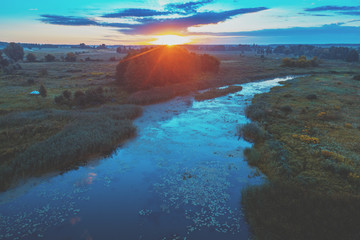 Naklejka premium Magical sunset over the countryside. River on the meadow. Rural landscape in the evening. Aerial view