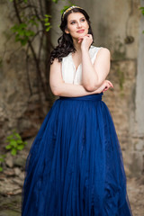 Fototapeta premium Tranquil Caucasian Lady in Long Blue Dress and Tiara Posing in Authentic Yard Outdoors.